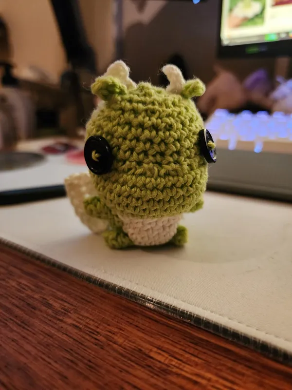 Green crochet dragon with button eyes.